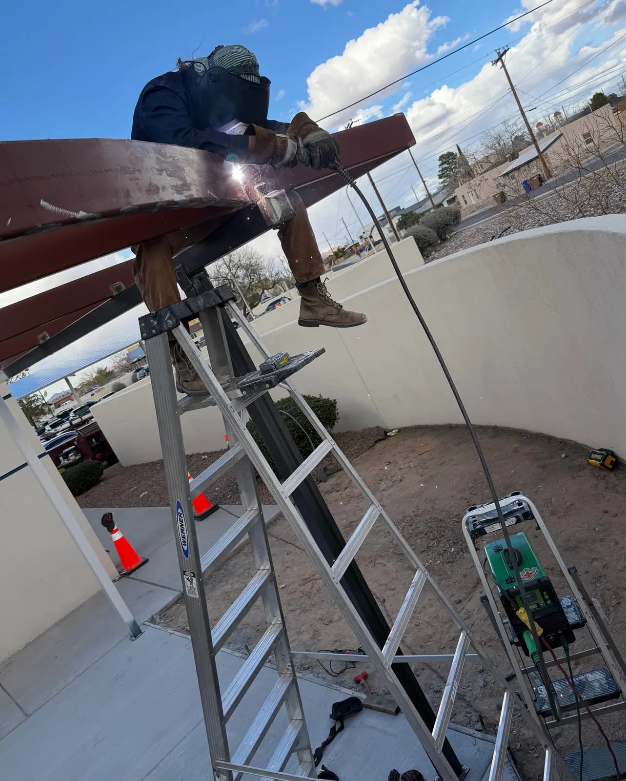 Welder welding a steel canopy beam on-site from a ladder in Las Cruces