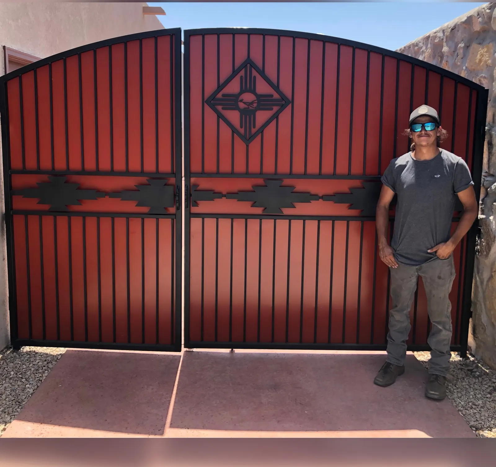 Red steel double driveway gate with a Zia diamond and Southwest step pattern
