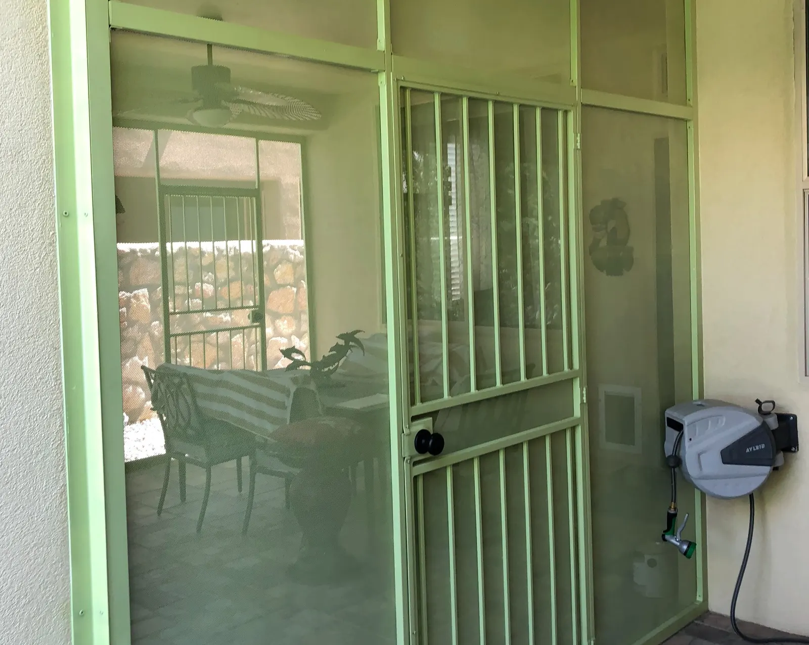 Screened porch enclosure with a barred steel door and green frame