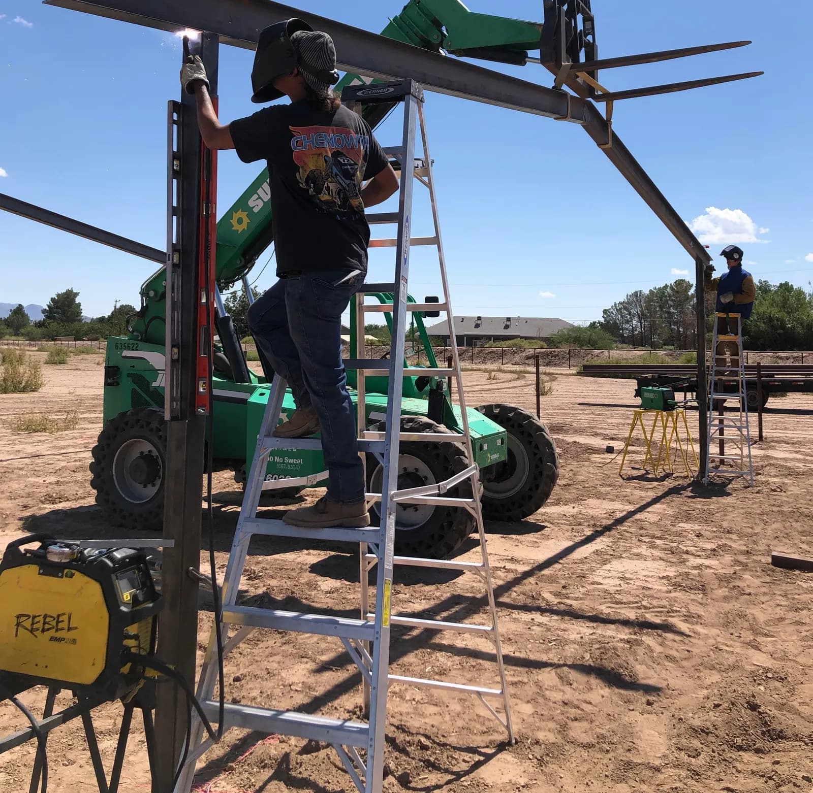 Welder setting a steel I-beam with a telehandler on a rural job site