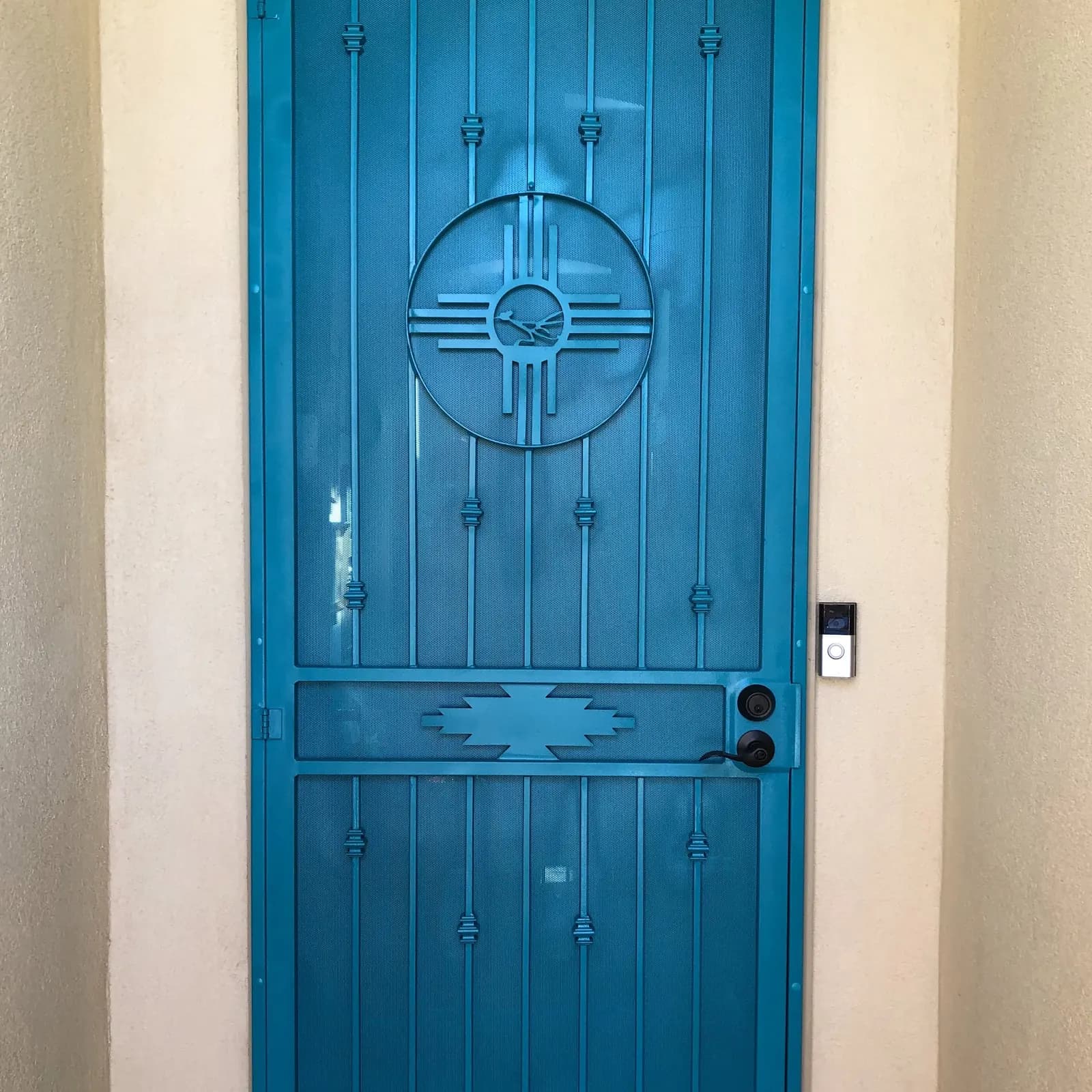 Turquoise steel security screen door with a Zia sun and Southwest step motif