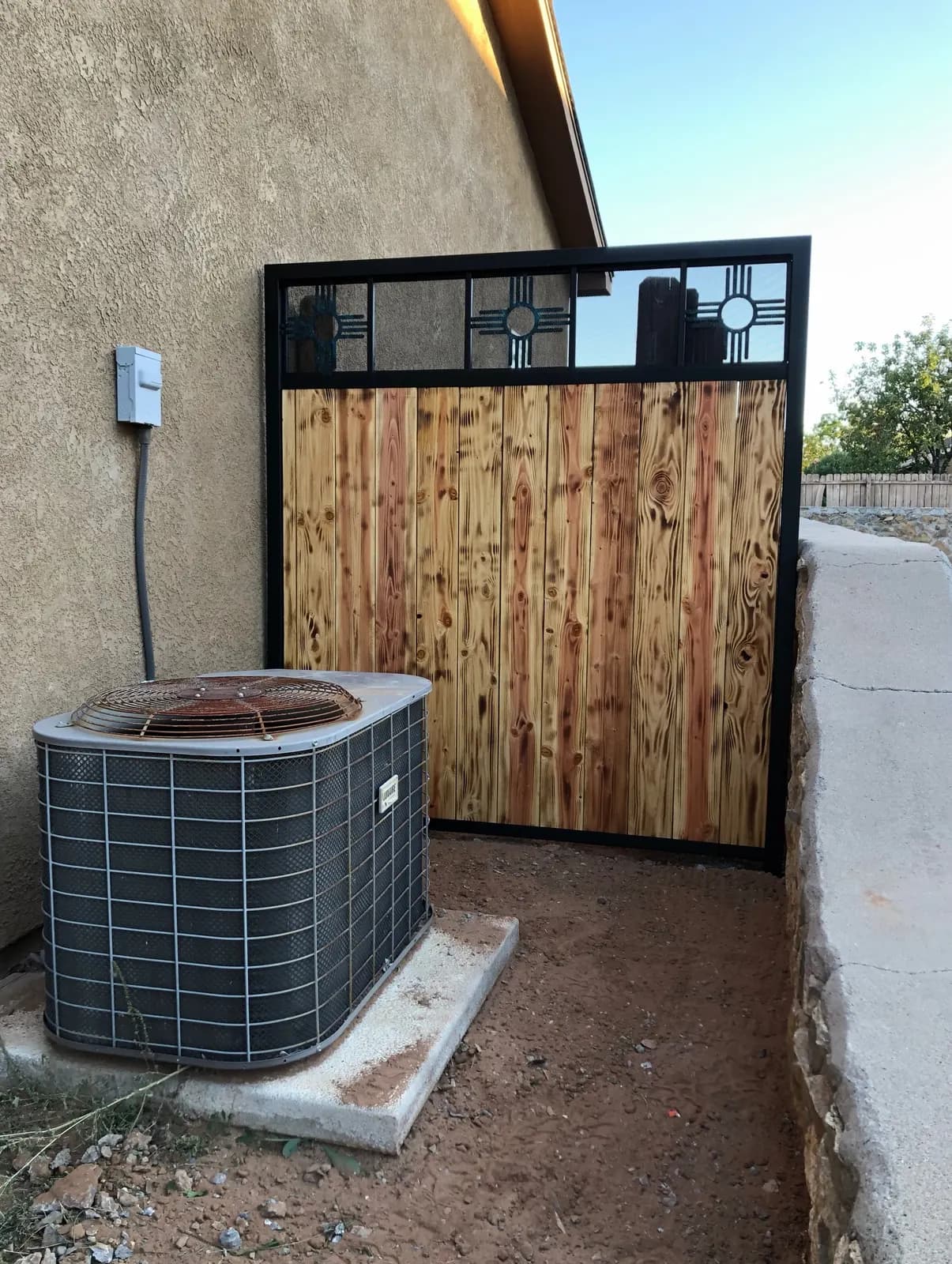 Wood and steel privacy screen hiding an AC unit beside a stucco home