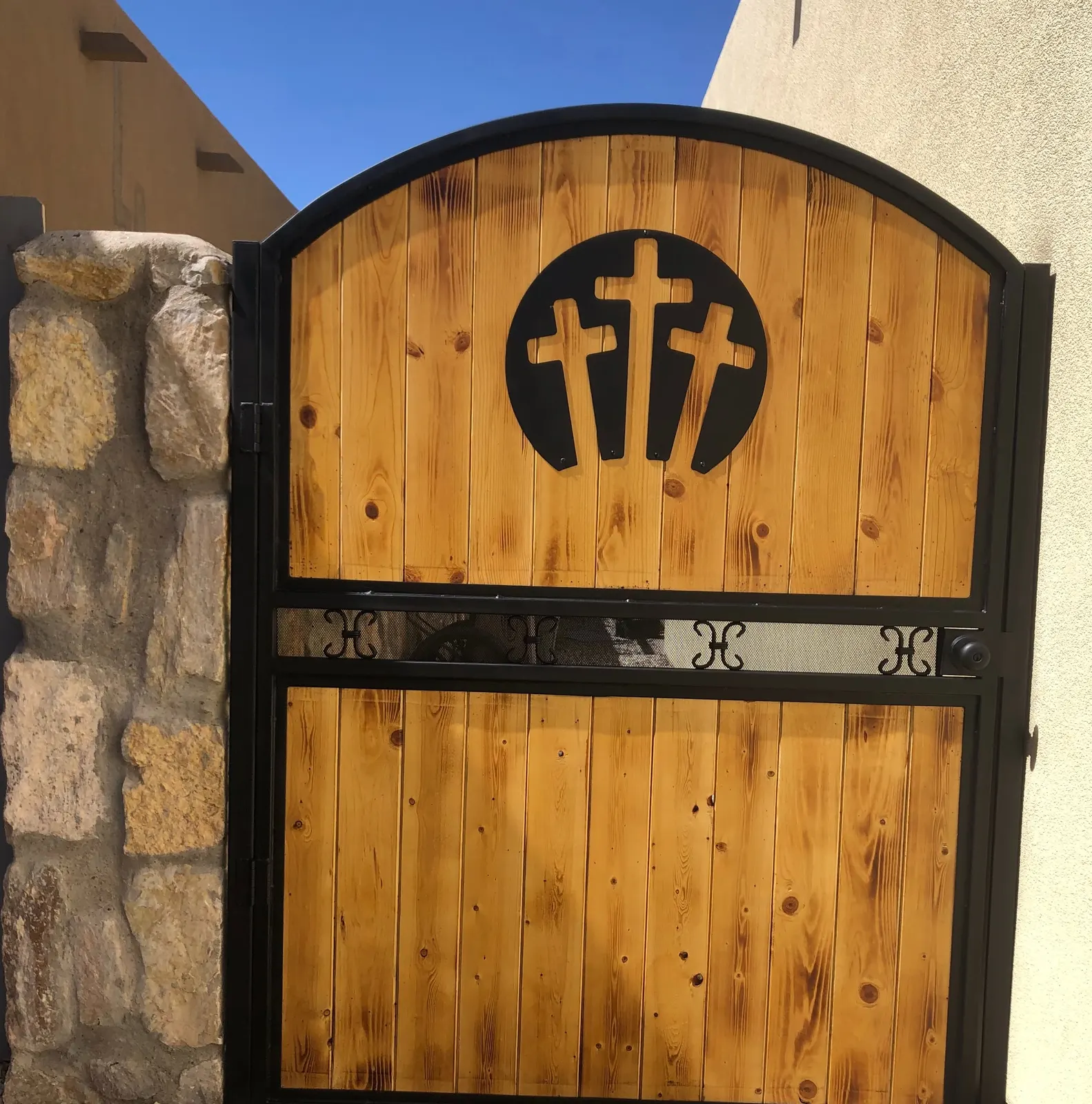 Arched wood and black steel gate with three crosses in a stone wall