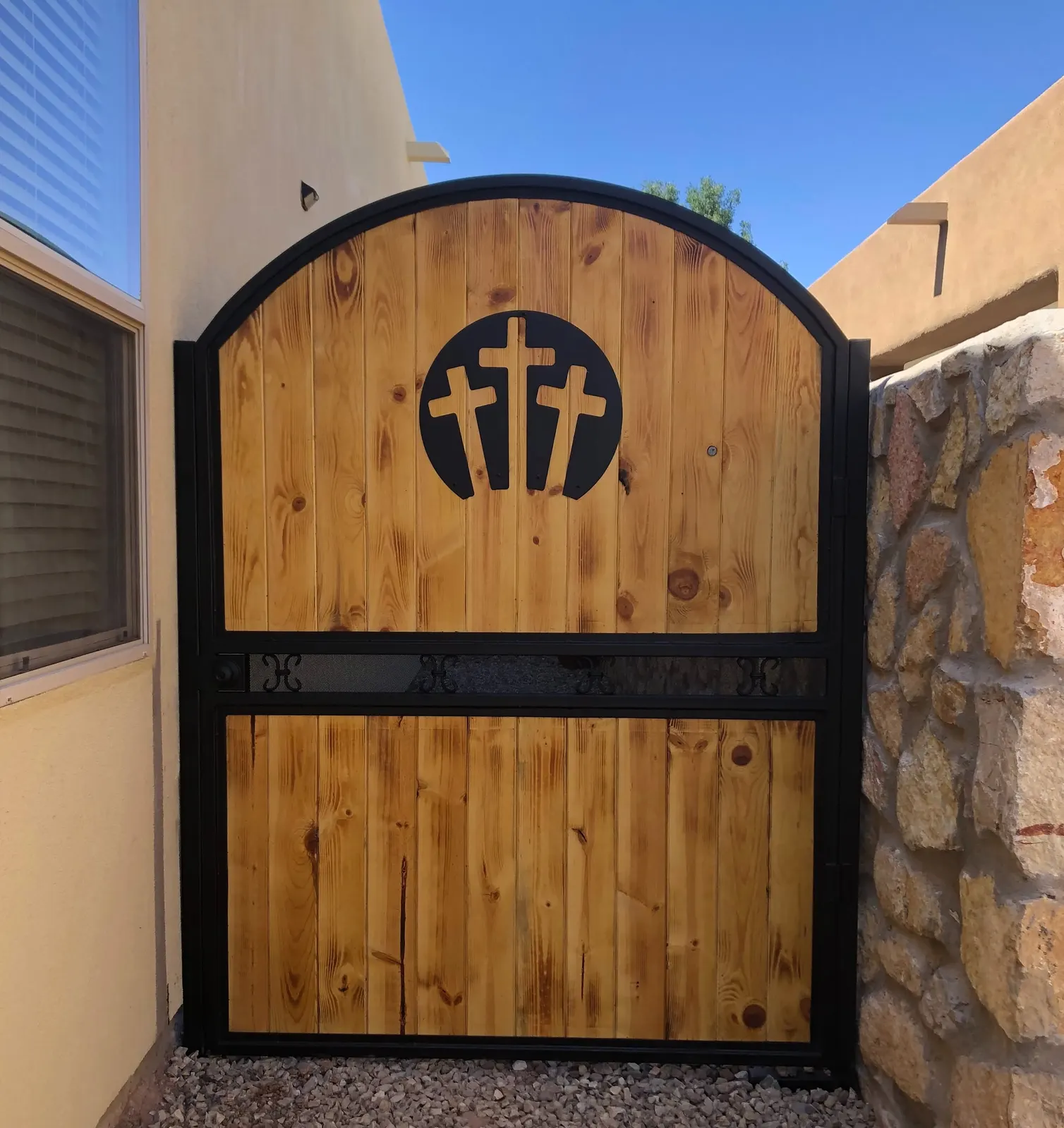 Arched wood-and-steel courtyard gate with a three-cross cutout