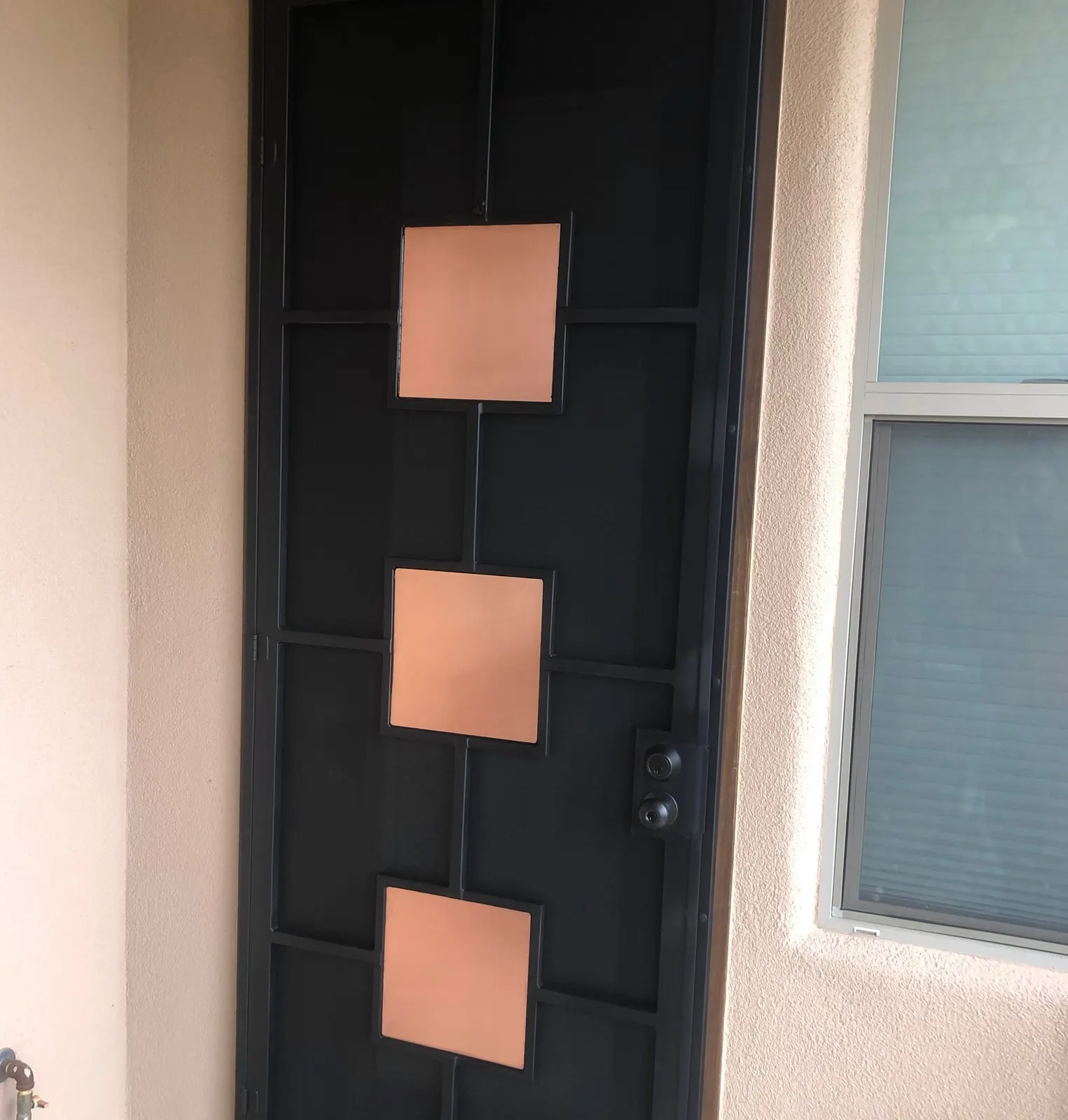Black security screen door with three copper squares on a stucco home