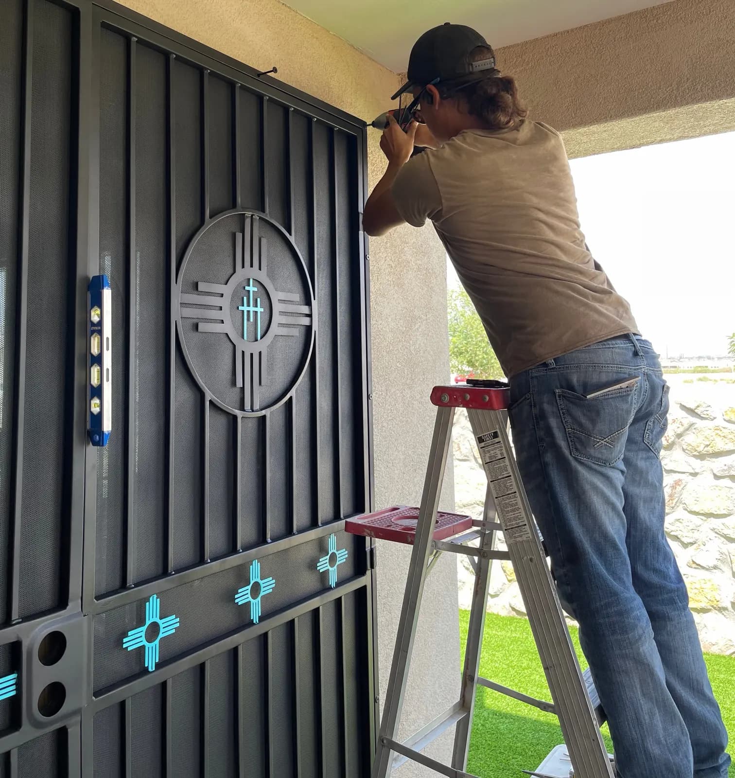 Installer leveling a black Zia security screen door with turquoise accents
