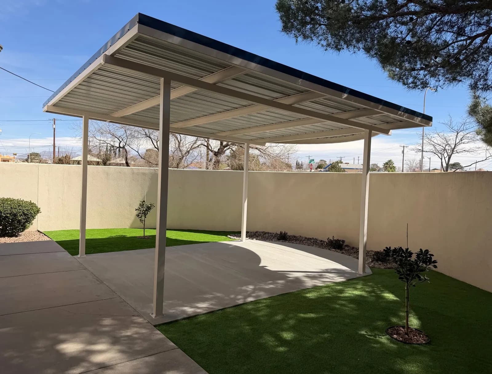 Metal shade canopy with white posts beside artificial turf in a courtyard