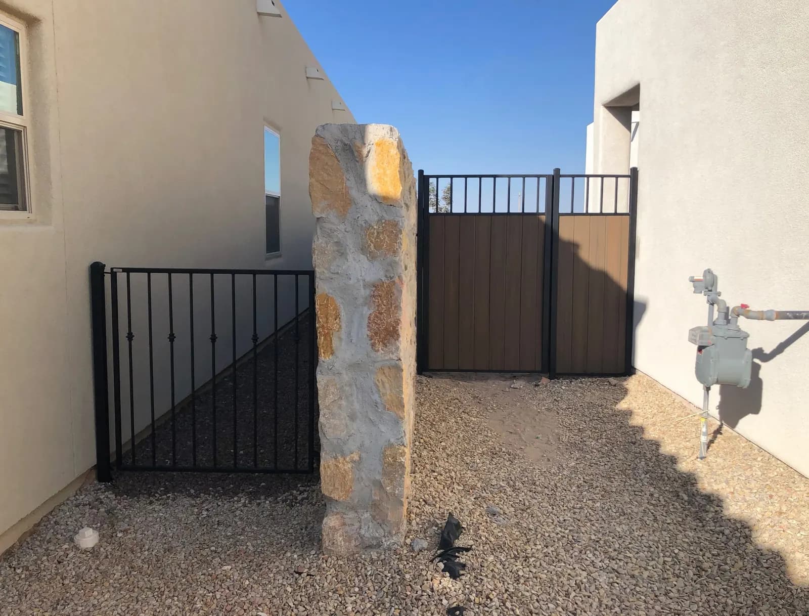 Side-yard wrought iron gate and composite privacy gate beside a stone pillar