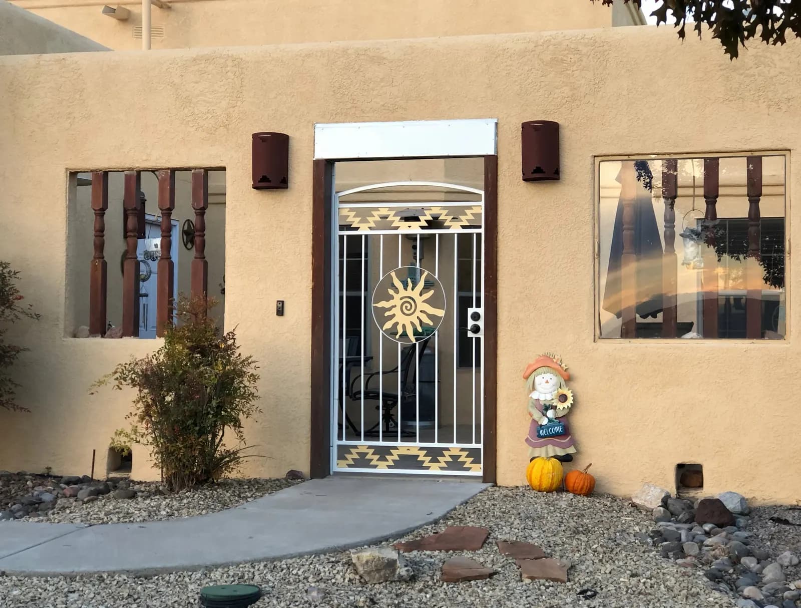 Southwest adobe home with a white steel courtyard gate featuring a gold sun and Native-pattern accents