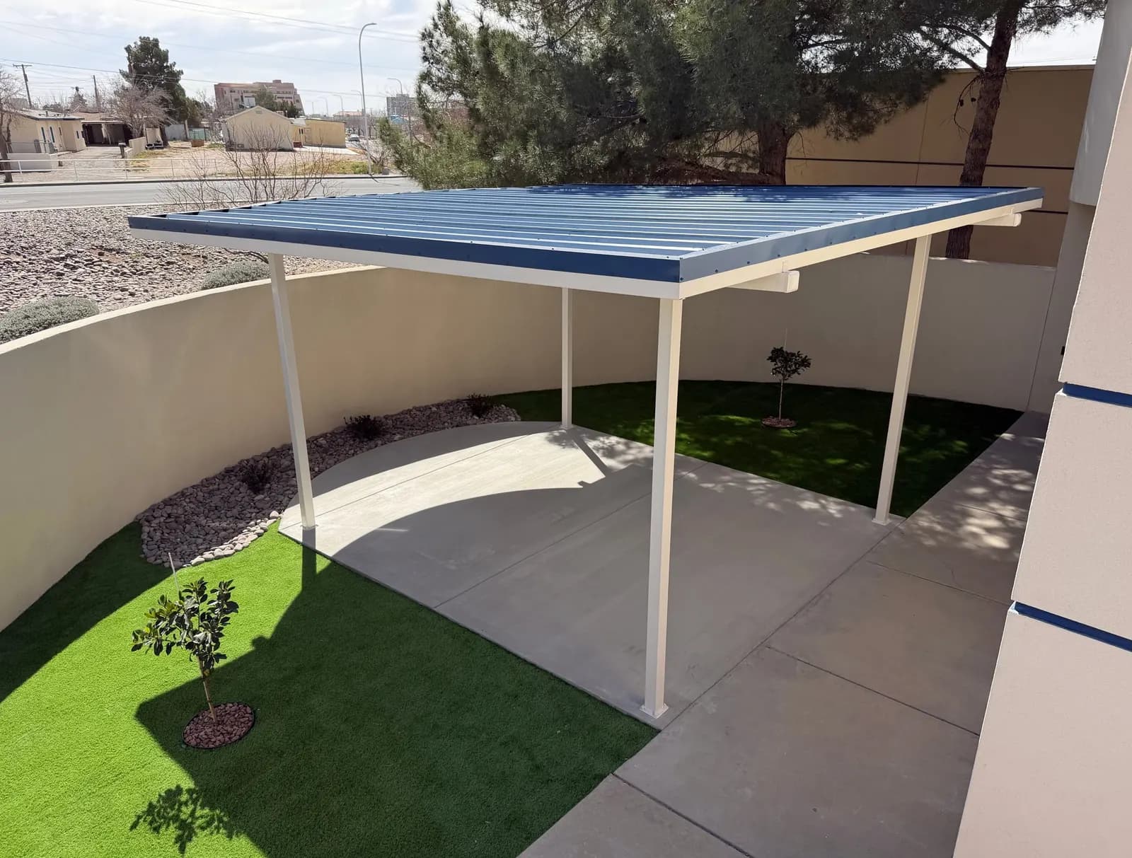Steel shade canopy following a curved stucco wall over turf and a walkway, Las Cruces