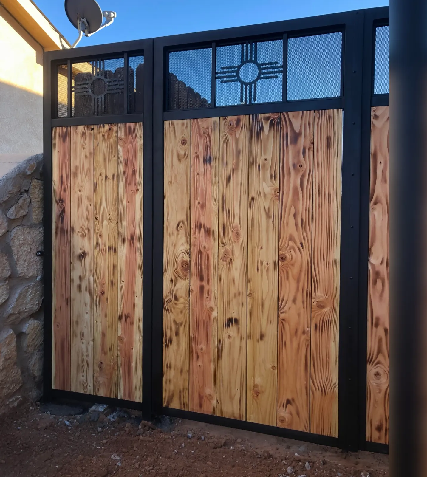 Wood and steel privacy screen along a side yard with a stone wall