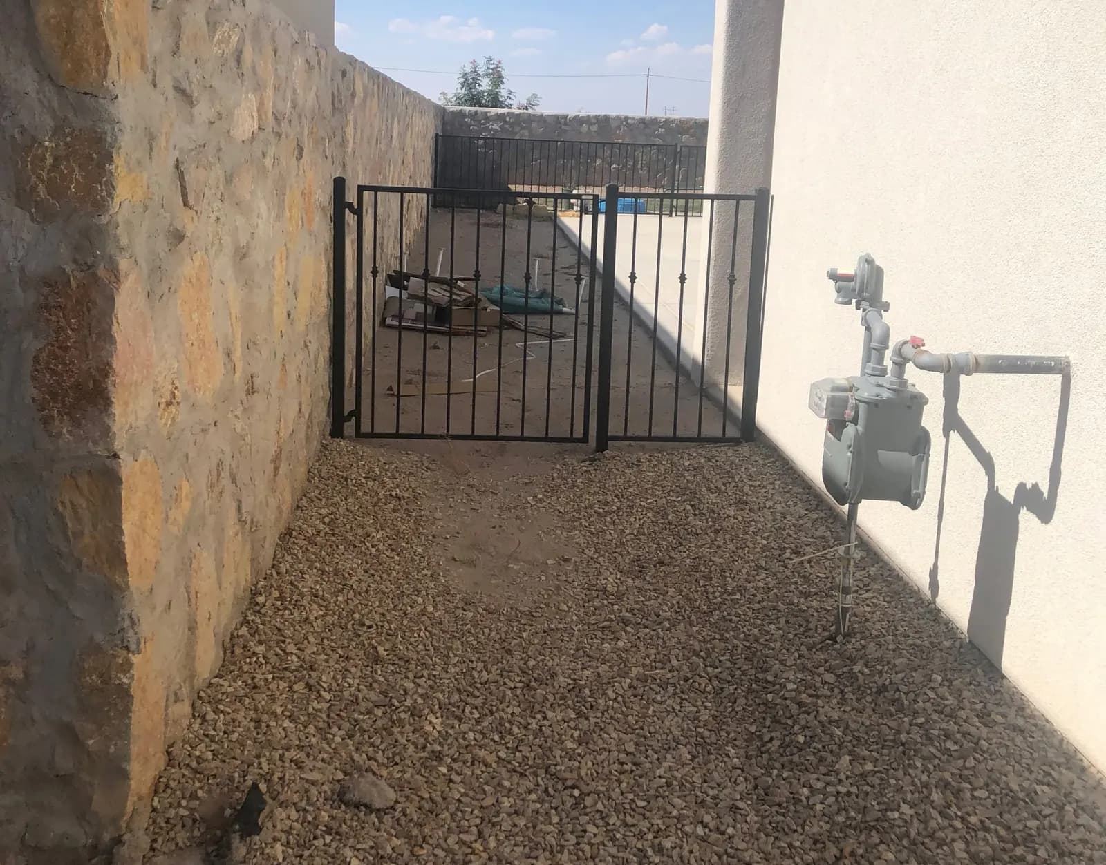 Black wrought iron side-yard gate between a stone wall and stucco home
