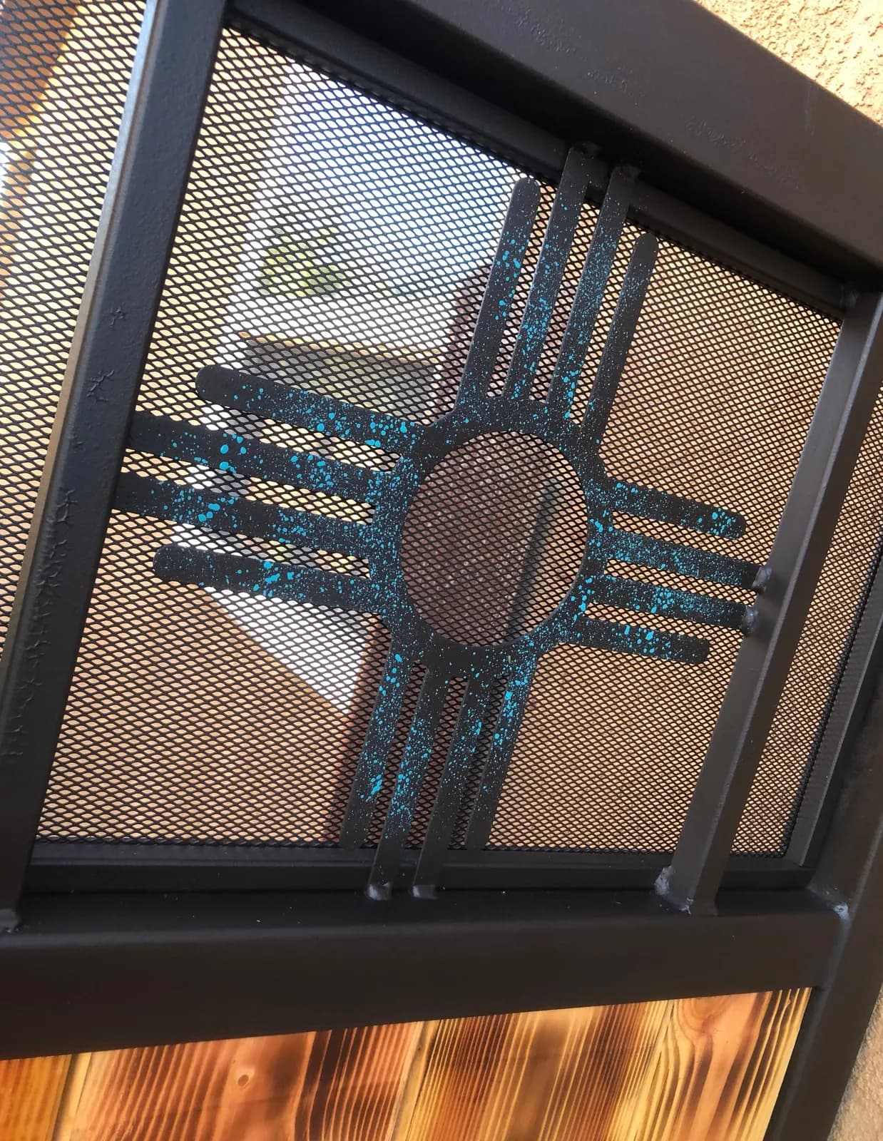 Close-up of a turquoise Zia sun cutout in a steel privacy screen