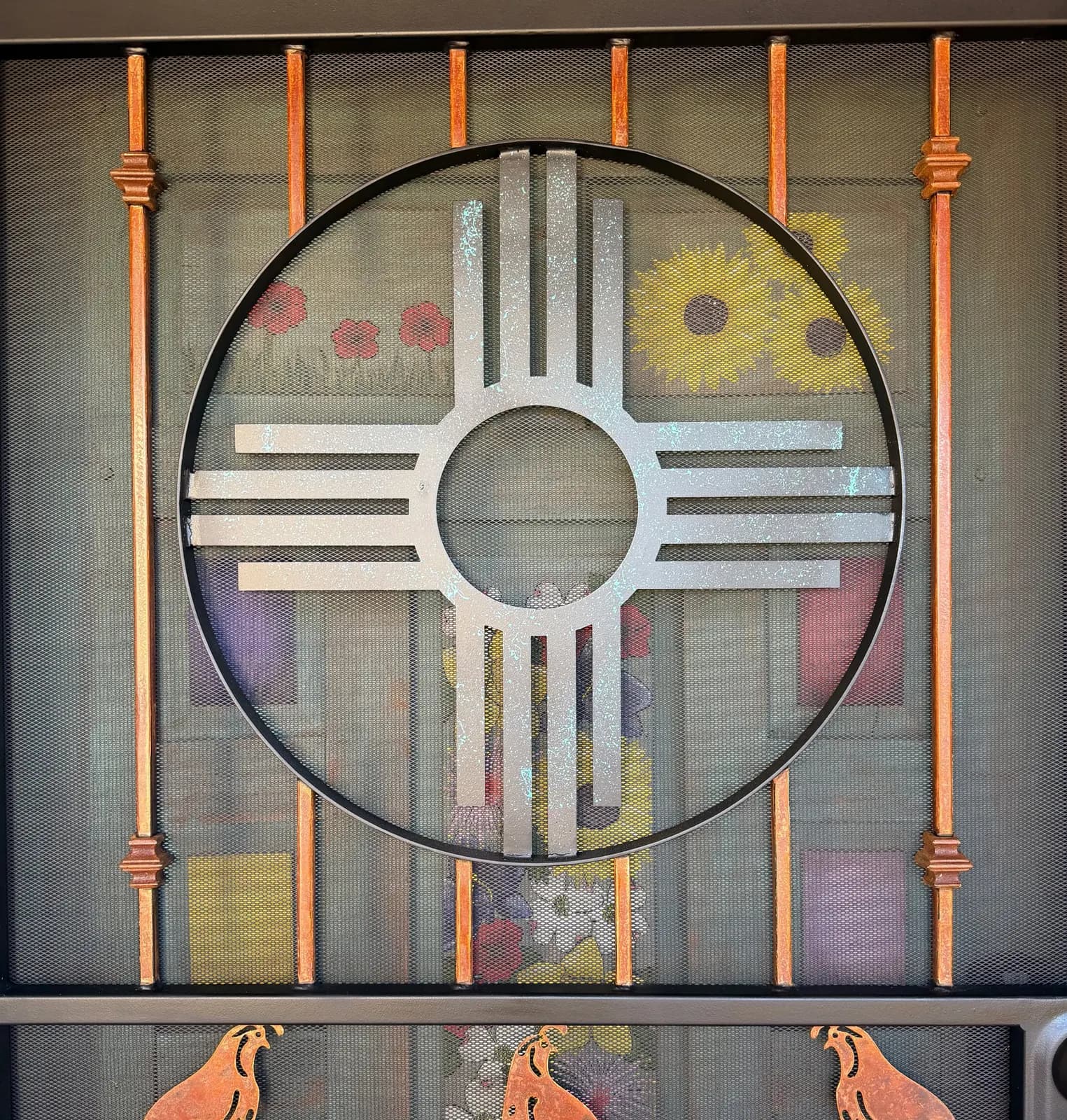 Close-up of a custom security screen door with a silver Zia sun, copper bars, and cut-steel quail